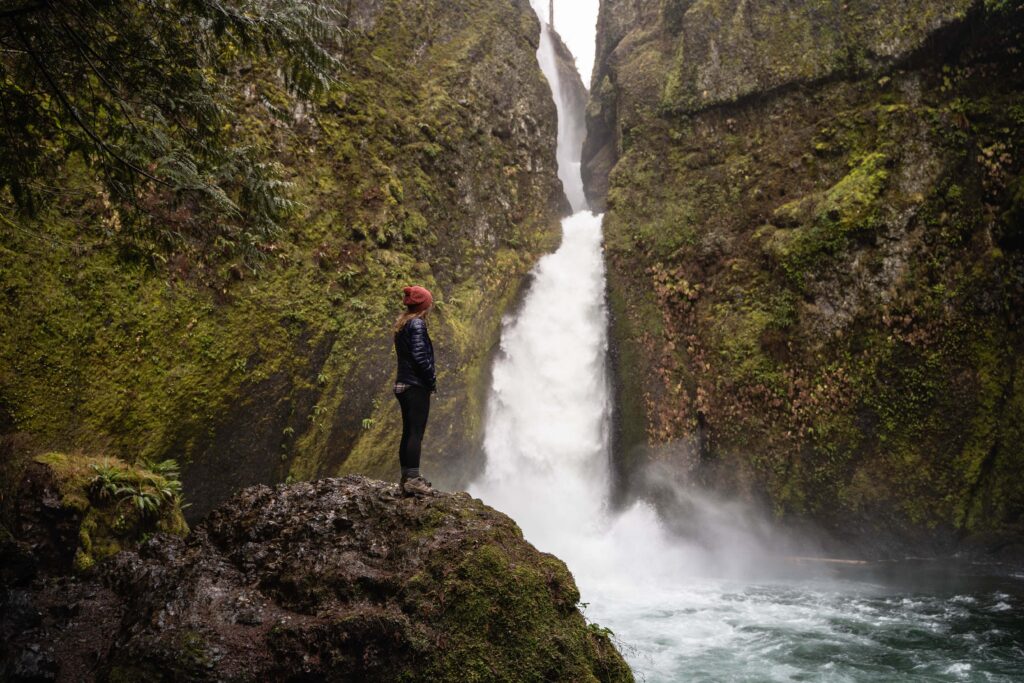 girl standing next to a raging waterfall in the Columbia River Gorge