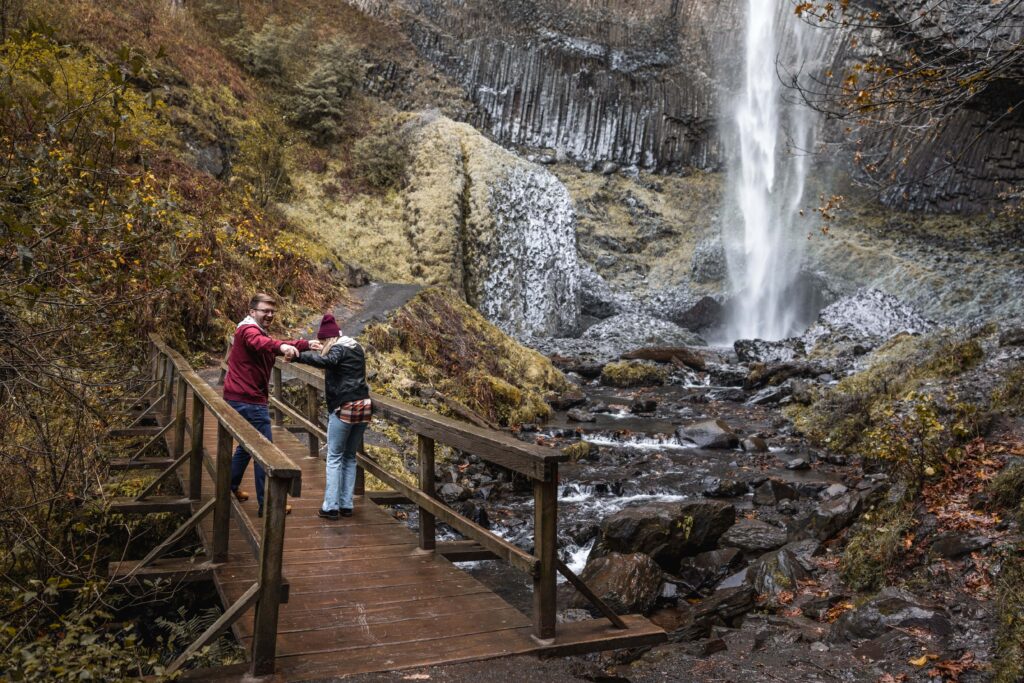 couple on bridge over creek by oregon waterfall