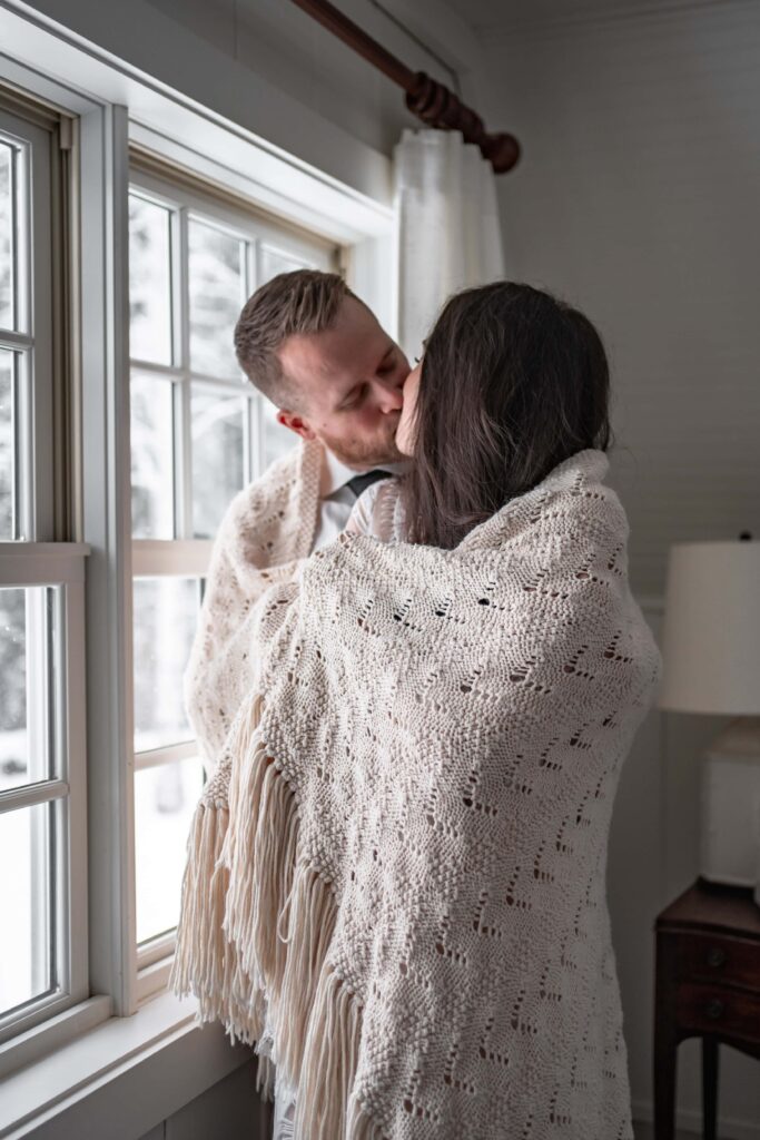 couple wrapped in white blanket cuddle in winter cabin