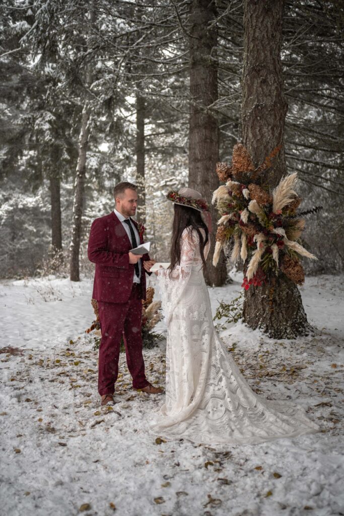 bride and groom read vows in winter forest elopement 