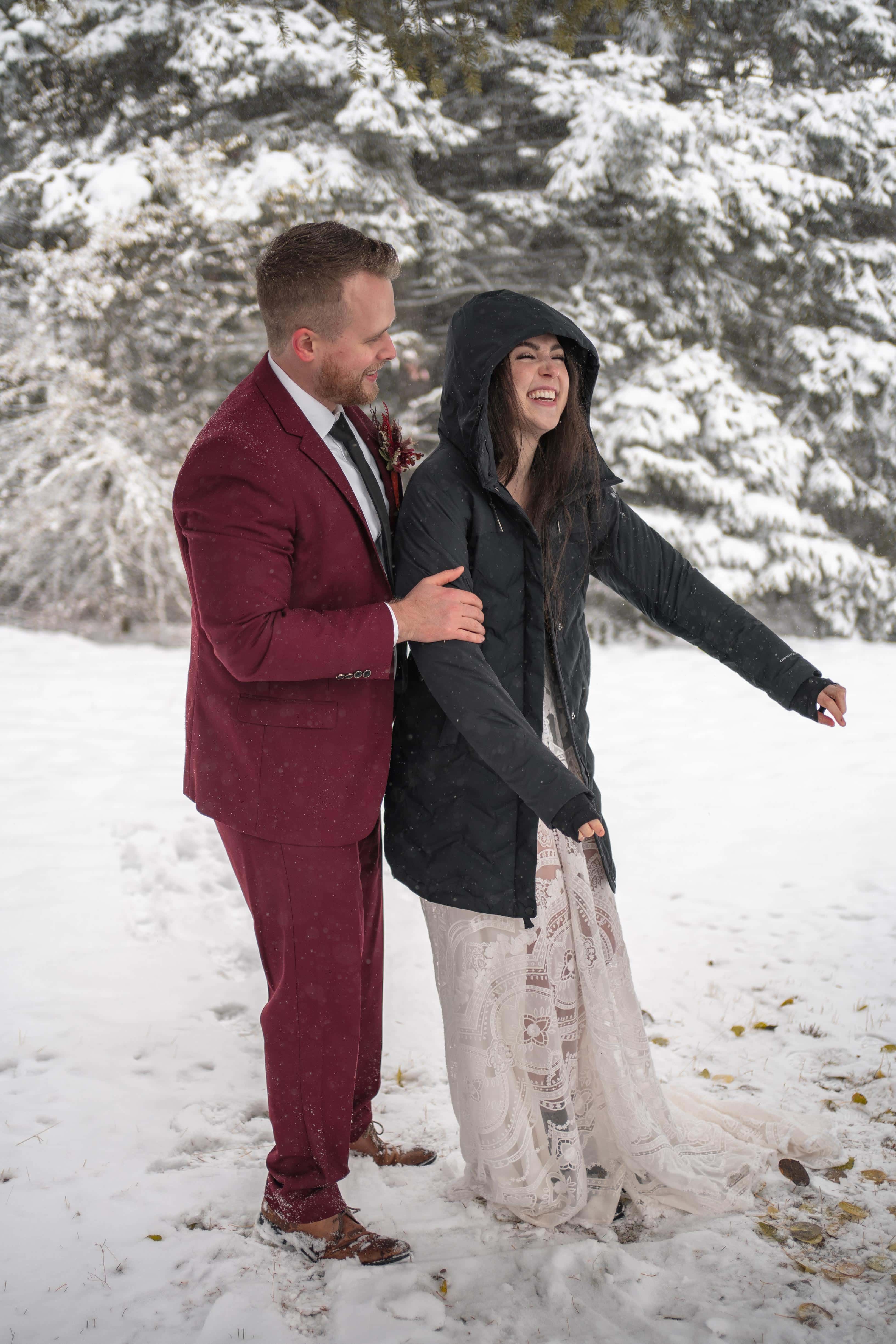 groom helps bride get ready for forest elopement in snow