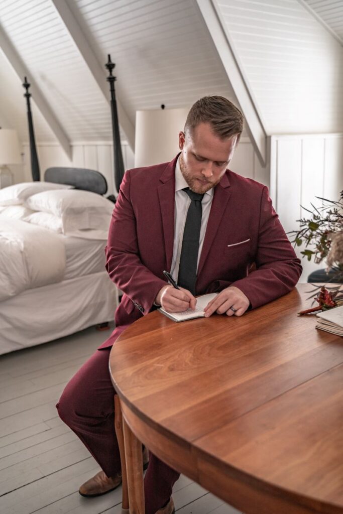 groom in red suit writing vows in small cabin in the mountains for Oregon elopement