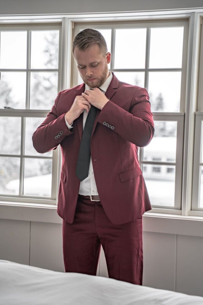 groom getting ready in maroon suit for winter elopement in the forest